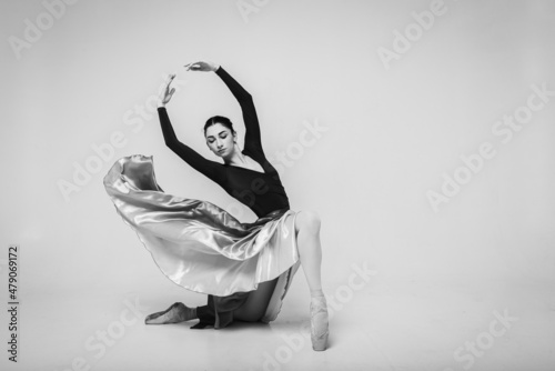 young pretty, beautiful ballerina dancing in a long dress on a light background isolated on a white background. Classical ballerina in pointe shoes and dress. Black and white photo