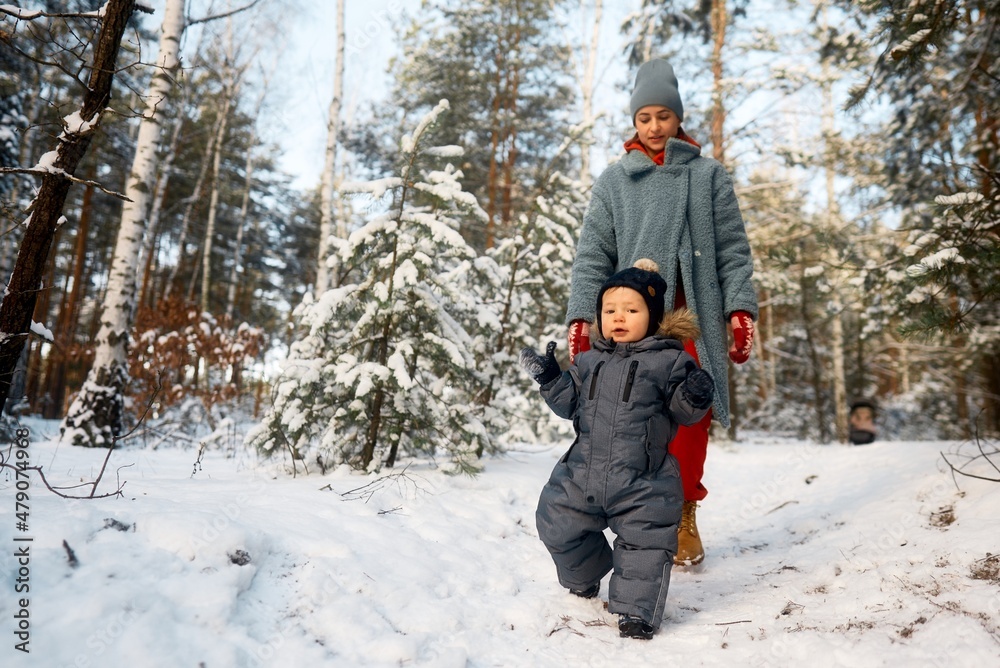 Young mother and her baby playing in the snowy forest. Young mother carrying her baby in the forest on a very snowy day. Young mother and her baby playing in the snowy forest. Young mother carrying her baby in the forest on a very snowy day.