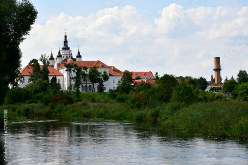 A view of several domes and towers of an old Orthodox monastery with many decorative elements seen in the middle of a small Polish village on a cloudy yet warm summer day during a hike
