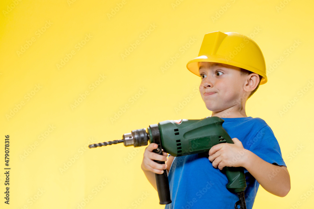 Cute boy in a construction helmet with a drill in his hands Cute boy in a construction helmet with a drill in his hands