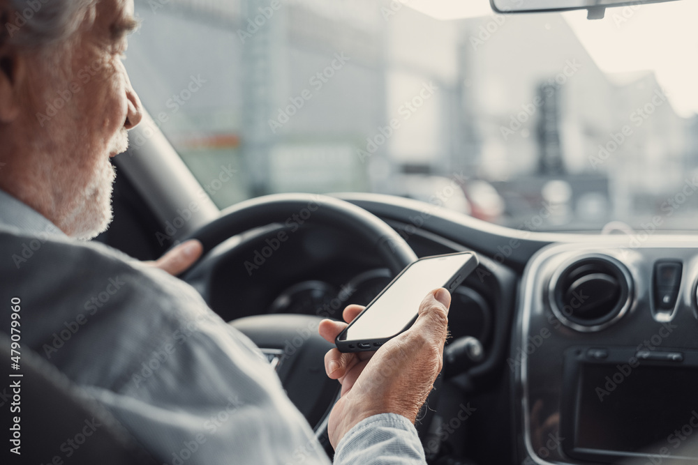 Man looking at mobile phone while driving a car. Old pensioner person distracting texting and chatting.. Man looking at mobile phone while driving a car. Old pensioner person distracting texting and chatting..