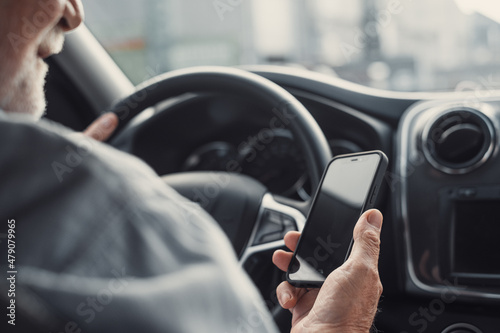 Man looking at mobile phone while driving a car. Old pensioner person distracting texting and chatting..