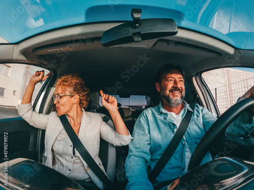 Couple of happy people dancing and singing in the car driving and traveling with a vehicle in the street enjoying their lifestyle having fun.