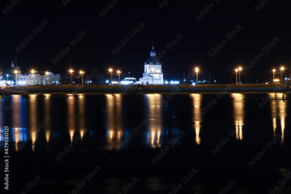 Night view in the Volga river bank with a view of the church and its reflections in the water.