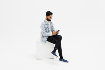 Young man sitting on chair while looking at phone celebrating on white background