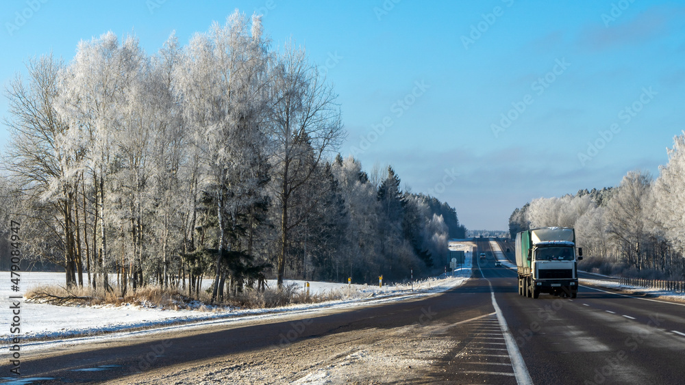 Truck goes on winter road. Van in the road of winter. Lorry car and cold landscape. Roadway and route snowy street trip.