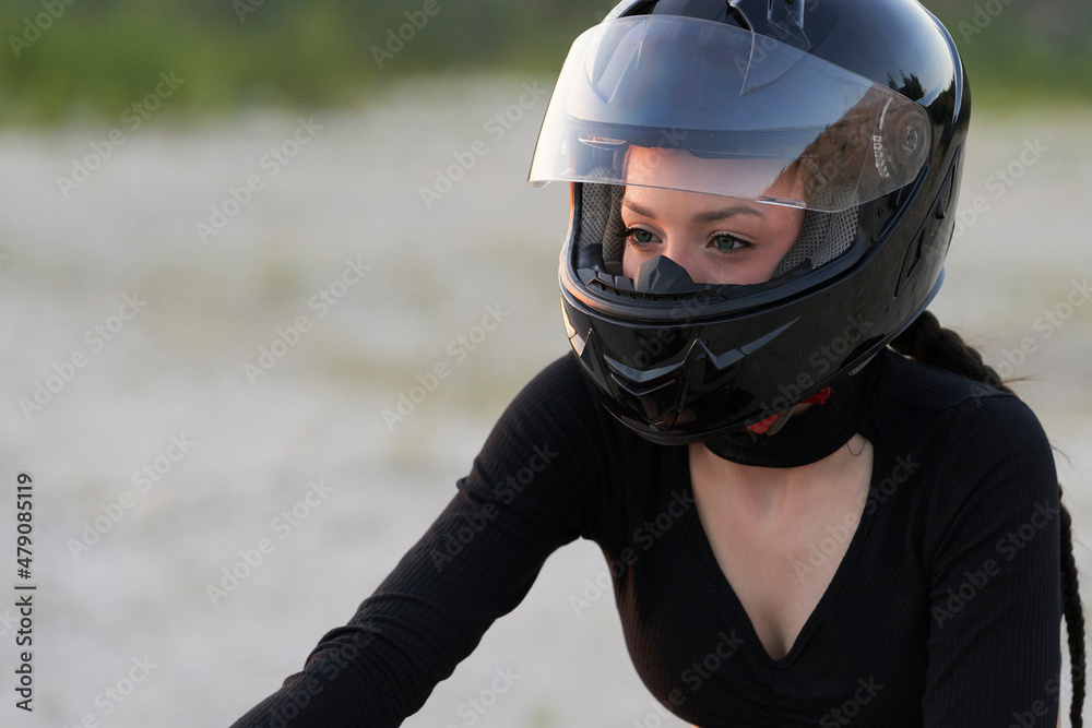 Portrait of a pretty biker girl in a protective helmet in nature. Selective focus. Copy space.