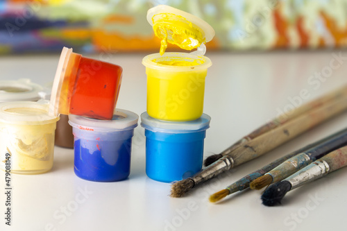 A group of small cans of paint by number and paint brushes. An open can of yellow paint, multi-colored plastic paint jars.
