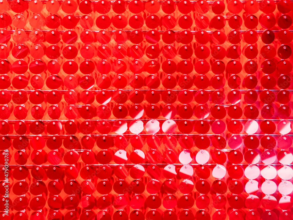 Full-framed background made of plastic spangles. Vibrant backdrop made of bright red round beads.