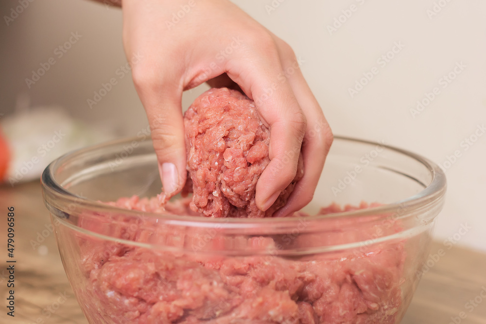 person taking raw minced beef, veal or pork to cook hamburgers fast food on a wooden table in the comfort of their home person taking raw minced beef, veal or pork to cook hamburgers fast food on a wooden table in the comfort of their home