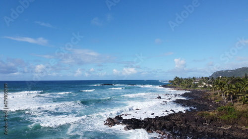 Oceanview coastline waves crashing into rocks blue clear skies landscape view drone in Hawaii