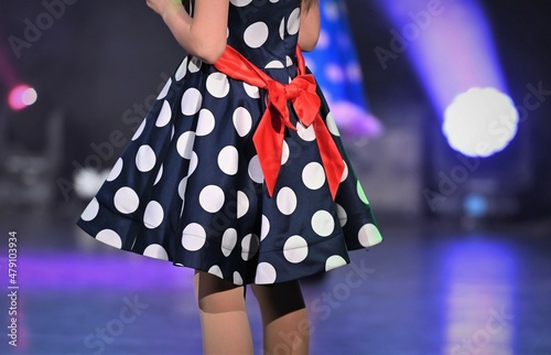 Dress with large polka dots, with a red bow on the back of the child on stage. The concept of a child's participation in a television show.