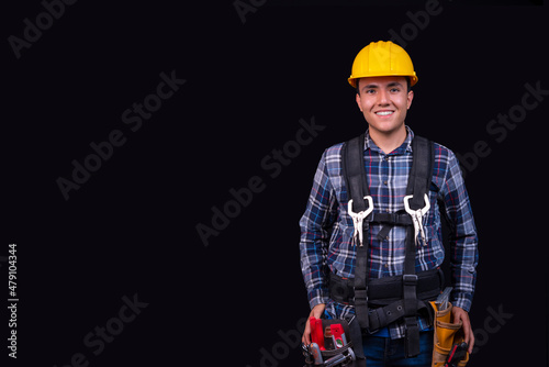 Young man smiling with his tools and safety equipment, on an isolated black background, copy paste, concept of safety at work