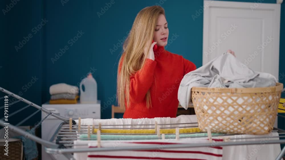 Young blonde woman talking on the smartphone hanging clothes on clothesline at laundry room Young blonde woman talking on the smartphone hanging clothes on clothesline at laundry room