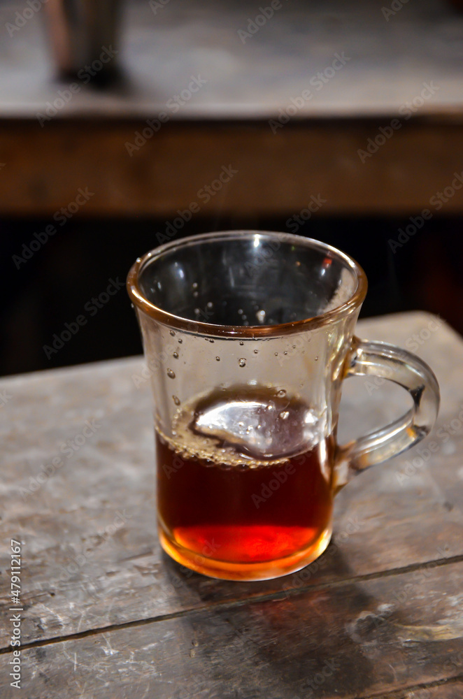 Closeup of a tea cup and half tea liquid inside. Glass cup and black tea on the table textured. Closeup of a tea cup and half tea liquid inside. Glass cup and black tea on the table textured.