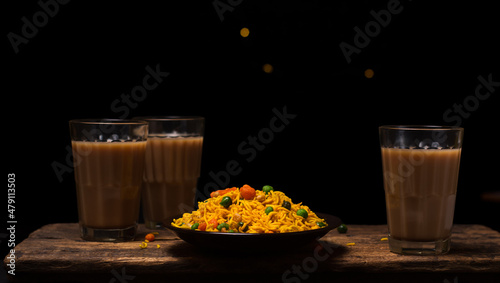 crispy and spicy masala mix chips, made with flour, green peas, fried lentils, nuts and rice puffs, quick snack on a plate, with glass of tea, on a dark background
