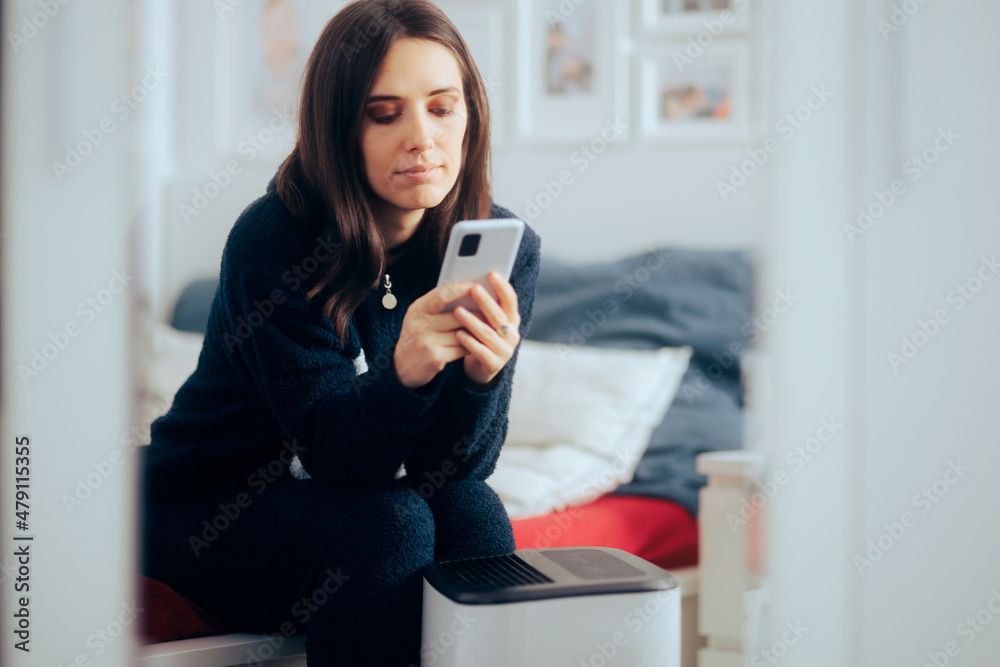 Woman Controlling Humidity and temperature in the room with smart-phone app Woman Controlling Humidity and temperature in the room with smart-phone app