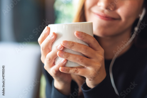 Closeup of a young woman drinking coffee while putting on an earphone to listen to music
