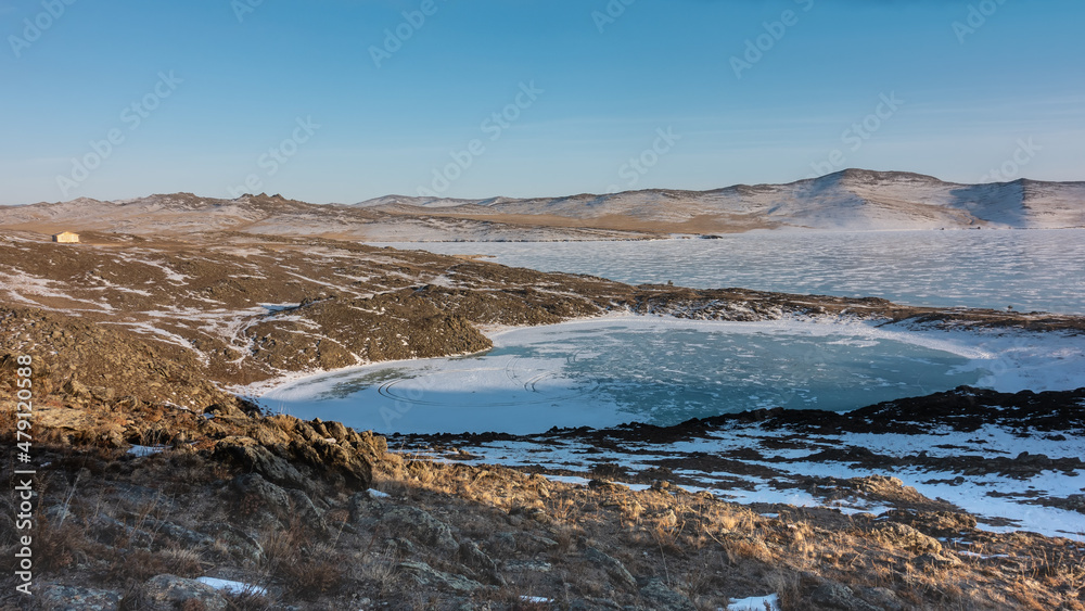 A small frozen lake in the shape of a heart and a large one next to it. There are tire tracks on the ice. Snow and dry grass on cold ground. A lonely house on a hill. Blue sky. Siberia A small frozen lake in the shape of a heart and a large one next to it. There are tire tracks on the ice. Snow and dry grass on cold ground. A lonely house on a hill. Blue sky. Siberia