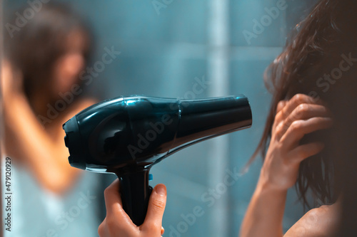 Girl is using hairdryer near the mirror, closeup. photo