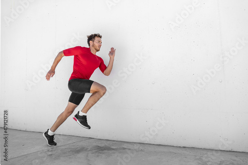 Sport athlete training running fast with explosive sprint for competition. Man runner working out at fitness gym outdoor white wall background. © Maridav