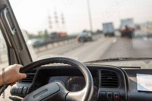 Male drives hands are holding steering wheel of truck during the movement in the road. Image with selective focus on the wheel, dashboard and blurred windshield