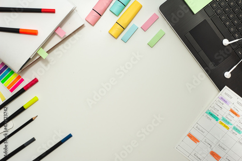 Colorful stationery, a school schedule and a cup of cocoa are laid out on a white table. Flat lay. Copy space