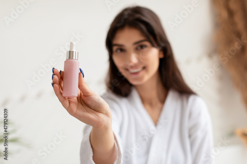 Brunette Woman Showing Facial Serum Bottle In Bathroom