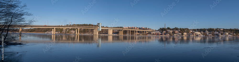 Panorama view over a long bridge at the frozen lake Mälaren, houses and a modern church, a sunny and snowy winter day in Stockholm