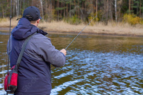 Fisherman with a fishing rod. Close-up - a fisherman stands on the shore with a fishing rod, catching fish. Colorful view, blurred background, selective focus. © Виктор Лазарев