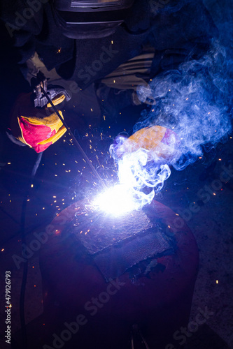 Fototapeta Naklejka Na Ścianę i Meble -  A welder in a workshop with a welding machine, welds metal structures. A worker in a factory uses a welding mask, tools and metalworking equipment.