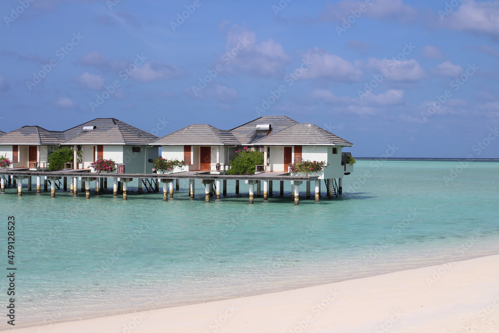 Morning in the Maldives, Indian Ocean shore with white sand, corals and villas over azure water Morning in the Maldives, Indian Ocean shore with white sand, corals and villas over azure water