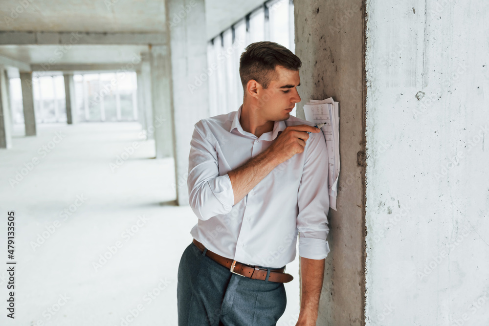 Documents on the pillar. Young man in formal wear is working indoors on the construction Documents on the pillar. Young man in formal wear is working indoors on the construction