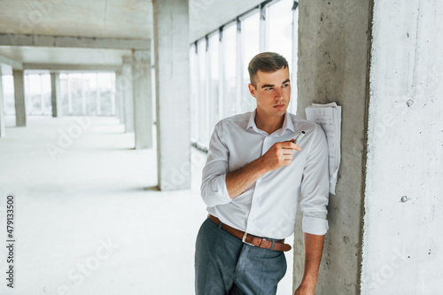 Leaning on the pillar. Young man in formal wear is working indoors on the construction © standret