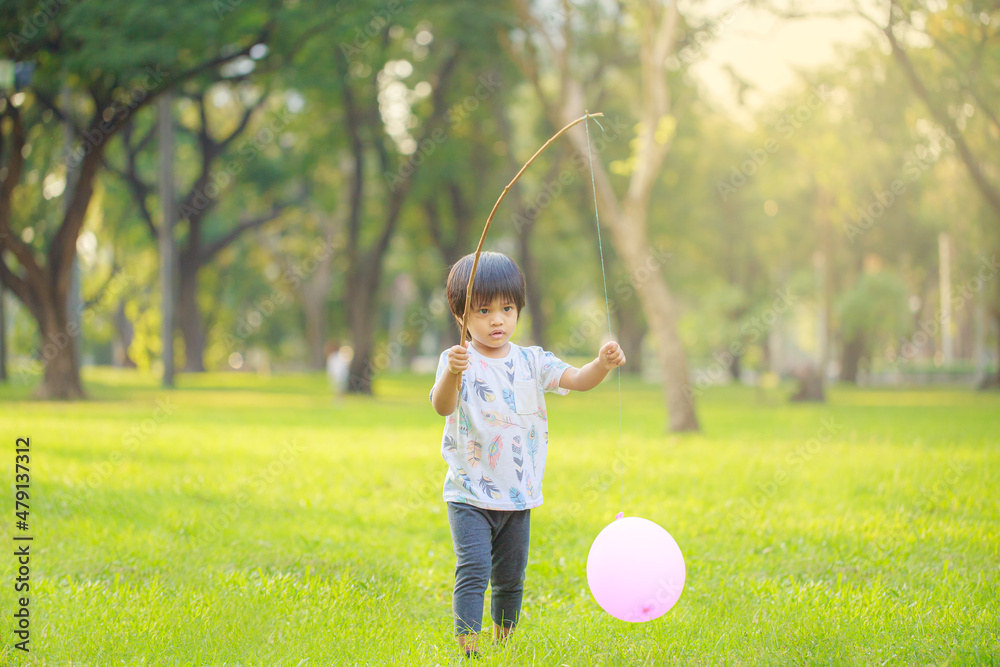 A happy Asian child with colorful toy balloons outside the house. Smiling child having fun in green spring field on blue sky background. freedom concept A happy Asian child with colorful toy balloons outside the house. Smiling child having fun in green spring field on blue sky background. freedom concept