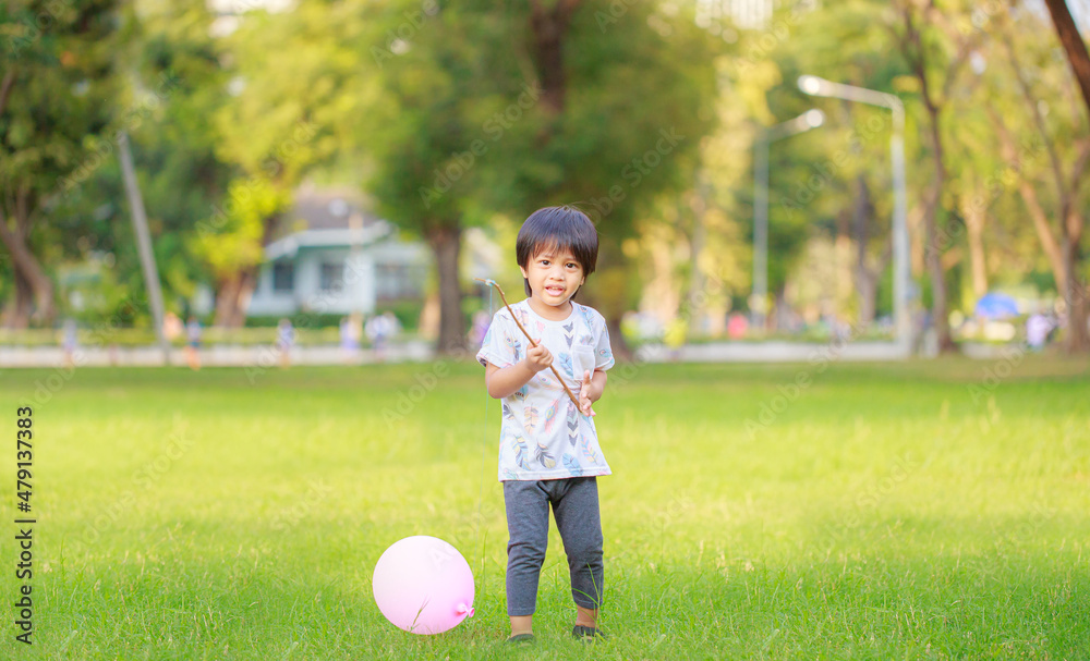 A happy Asian child with colorful toy balloons outside the house. Smiling child having fun in green spring field on blue sky background. freedom concept A happy Asian child with colorful toy balloons outside the house. Smiling child having fun in green spring field on blue sky background. freedom concept