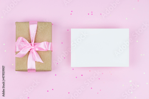 Blank paper card mock up on pink background with present and pink heart shape confetti © Eugenia