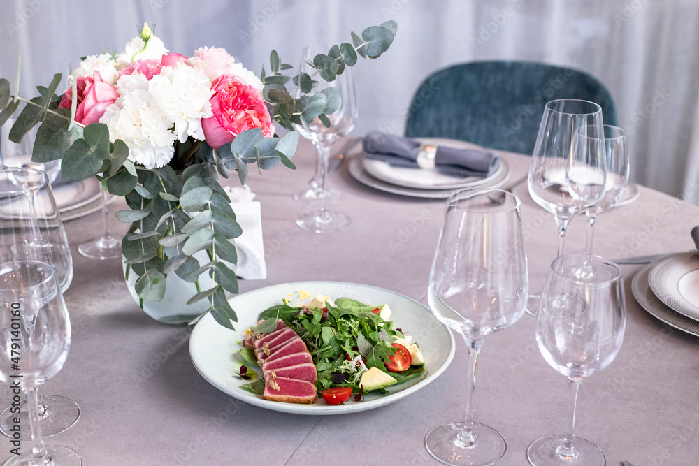 tuna salad on the serving table with wine glasses and flowers. grey tablewear. selective focus