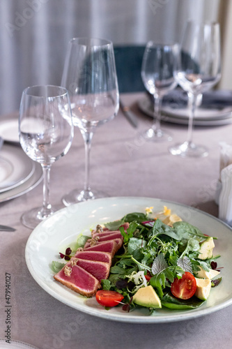 tuna salad on the serving table with wine glasses and flowers. grey tablewear. selective focus
