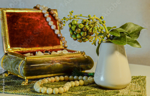 .In a vase there is a sprig of an ornamental shrub with fruits and leaves. There is a box with beads nearby.