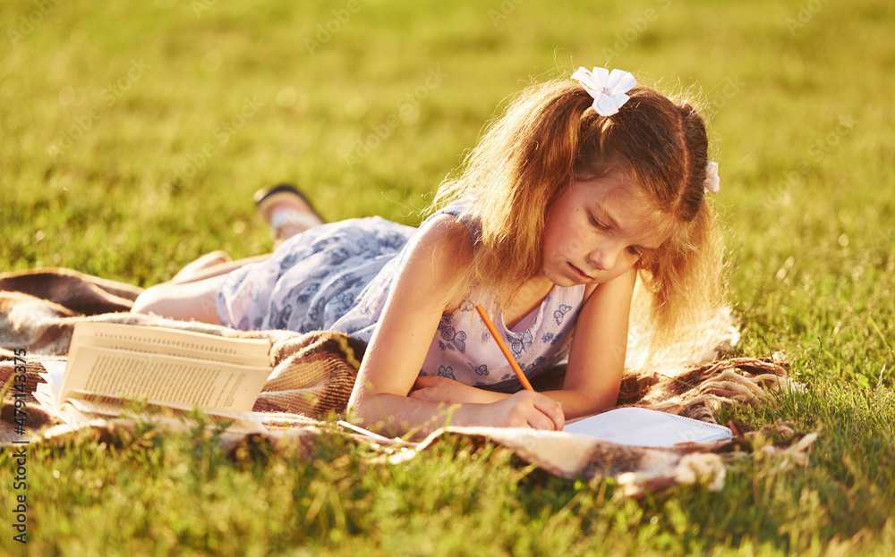 Little girl is reading book while laying down on the grass of field outdoors Little girl is reading book while laying down on the grass of field outdoors