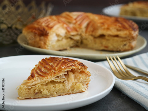 A cut piece of traditional French galette des rois or King cake with crown, it's a cake made with puff pastry and creamy almond filling roll in a circles shape. It's a cake associated with Epiphany 