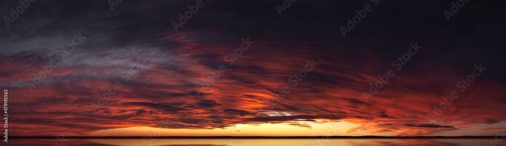 Sunset from bright saturated clouds. Dramatic sunset-sunrise with a pronounced texture of clouds and reflections on the horizon. Panorama of the evening sky with rich contrast of colors