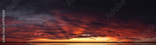 Sunset from bright saturated clouds. Dramatic sunset-sunrise with a pronounced texture of clouds and reflections on the horizon. Panorama of the evening sky with rich contrast of colors