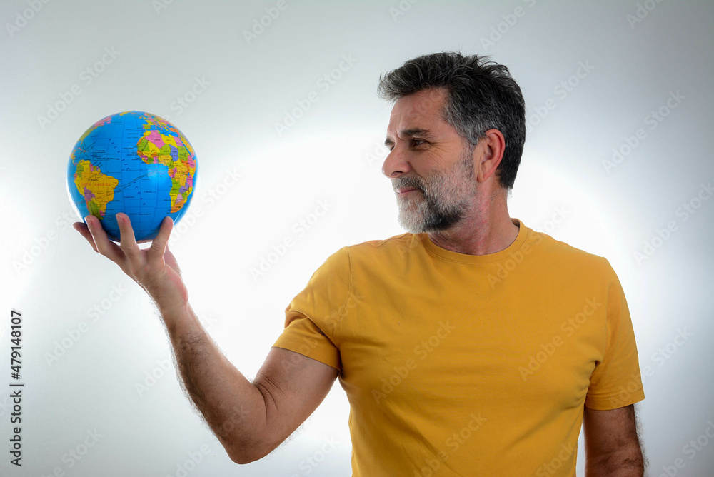 Happy cool mature bearded man with a world globe in hand. Senior man wants to explore unknown places, looks at worldwide globe, tries to choose destination, isolated over white background. Happy cool mature bearded man with a world globe in hand. Senior man wants to explore unknown places, looks at worldwide globe, tries to choose destination, isolated over white background.