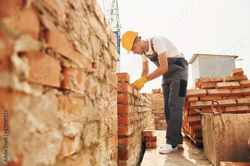 Using bricks. Young construction worker in uniform is busy at the unfinished building