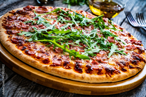 Circle pizza with mozzarella, pork ham and arugula on wooden table 