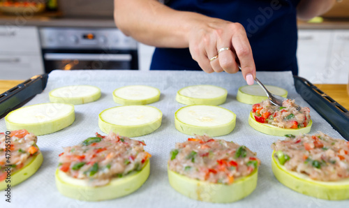 Zucchini stuffed with raw minced meat and vegetables on a baking sheet. female hands spread the minced meat on zucchini circles. The process of making dinner. close up