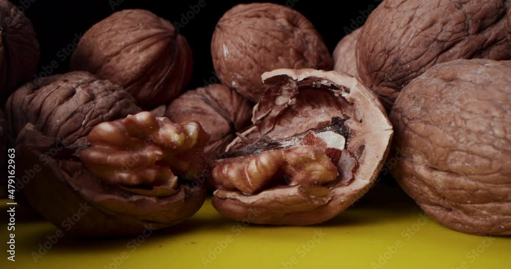 Close-up Shot of Walnuts which lie on a yellow table against a black background. Close-up camera travel along the lying nuts as close as possible to the chopped walnut. Close-up Shot of Walnuts which lie on a yellow table against a black background. Close-up camera travel along the lying nuts as close as possible to the chopped walnut.