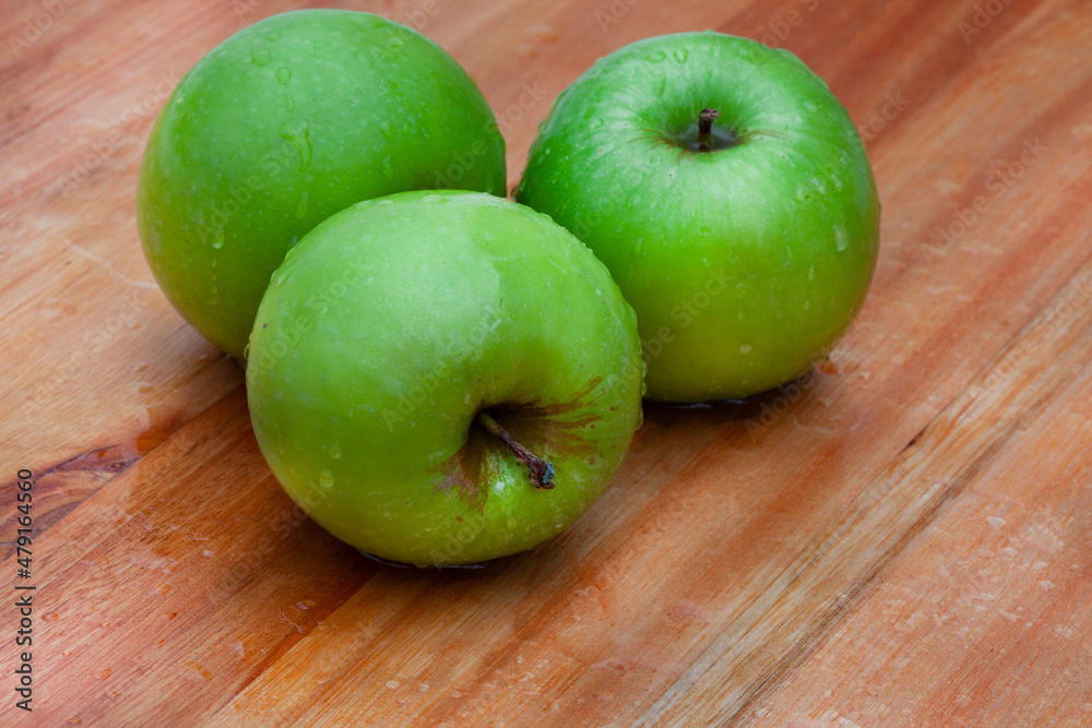 fresh and crisp green granny smith apples on wooden surface with water droplets fresh and crisp green granny smith apples on wooden surface with water droplets